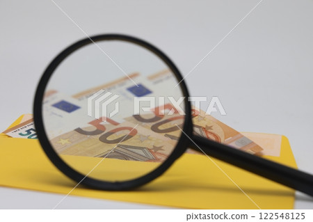 Banknotes in a yellow envelope and a magnifying glass on a white background Banknotes in a yellow envelope and a magnifying glass on a white background 122548125