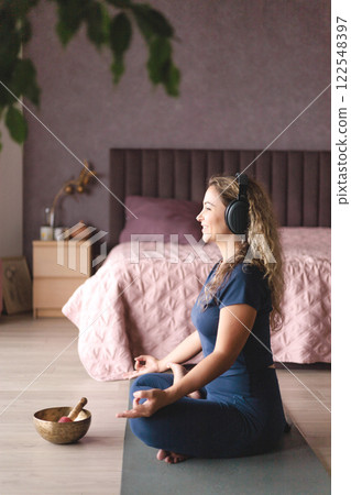 Smiling yoga woman meditation in lotus position listening music use headphones at home Smiling yoga woman meditation in lotus position listening music use headphones at home 122548397