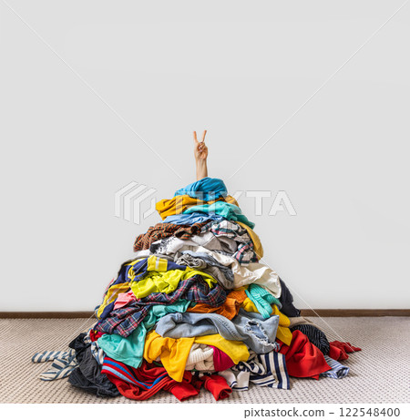 Unrecognizable human raises arm reaches out heap of colorful unfolded clothes busy doing wardrobe  122548400
