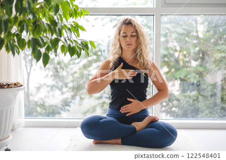 Woman yoga meditation sitting in lotus position near panorama window with houseplant at home Woman yoga meditation sitting in lotus position near panorama window with houseplant at home 122548401