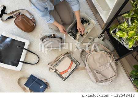 A young woman puts various women's handbags for storage in her home wardrobe. Accessories and bags. 122548418