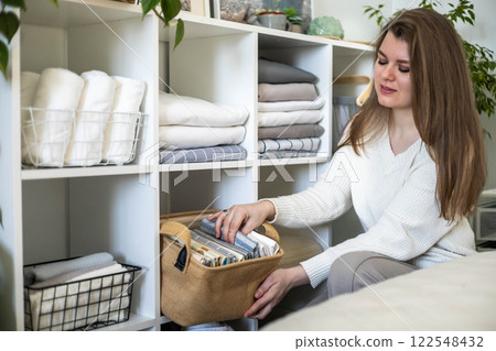 Modern housewife putting neatly folded towels, pillowcases, duvet covers into wicker basket Modern housewife putting neatly folded towels, pillowcases, duvet covers into wicker basket 122548432