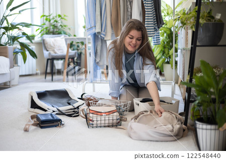 A young woman puts various women's handbags for storage in her home wardrobe. Accessories and bags. 122548440