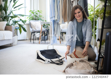 A young woman puts various women's handbags for storage in her home wardrobe. Accessories and bags. A young woman puts various women's handbags for storage in her home wardrobe. Accessories and bags. 122548447