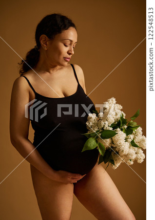 Pregnant woman in a black outfit holding white flowers on a neutral background Pregnant woman in a black outfit holding white flowers on a neutral background 122548513