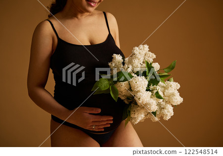 Pregnant woman holding flowers celebrating motherhood on a warm tonal background Pregnant woman holding flowers celebrating motherhood on a warm tonal background 122548514