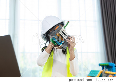 Girl child wear white hard hat assembling electric toys. Education STEM children student in classroom. Robot assembly training, brain development, Learning electrical future engineering. Girl child wear white hard hat assembling electric toys. Education STEM children student in classroom. Robot assembly training, brain development, Learning electrical future engineering. 122550536