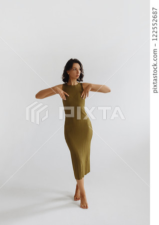 Young brunette woman gracefully poses in tight green dress on white background. 122552687