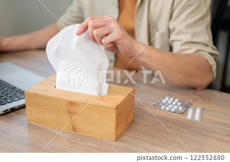 A close-up of a man reaching for a tissue from a tissue box while working at his desk in the office. A close-up of a man reaching for a tissue from a tissue box while working at his desk in the office. 122552880