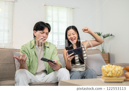 A lovely, joyful Asian couple enjoys racing a game on their smartphone, spending fun time together. A lovely, joyful Asian couple enjoys racing a game on their smartphone, spending fun time together. 122553113
