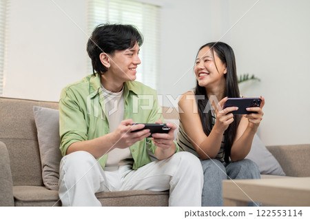 A lovely Asian couple enjoying playing a mobile game on their smartphones. A lovely Asian couple enjoying playing a mobile game on their smartphones. 122553114