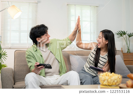 A cheerful couple give a high five to each other to celebrate after winning a game on their phones. A cheerful couple give a high five to each other to celebrate after winning a game on their phones. 122553116
