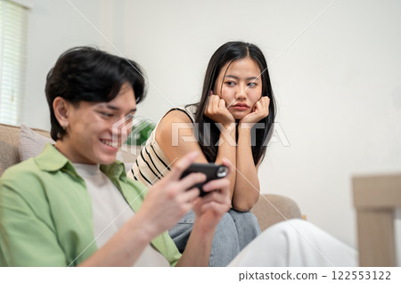 A moody Asian girl sits in the living room, feeling ignored by her boyfriend. 122553122