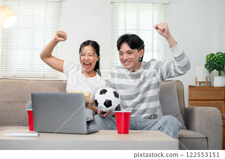 A happy Asian couple supporting their favorite team and enjoying watching the match together at home 122553151