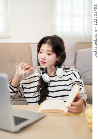 A thoughtful Asian female student is focusing on an online lecture as she studies from home. 122553401