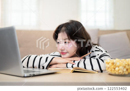 A tired Asian female student is resting her chin on her hands in front of her laptop while studying. 122553402