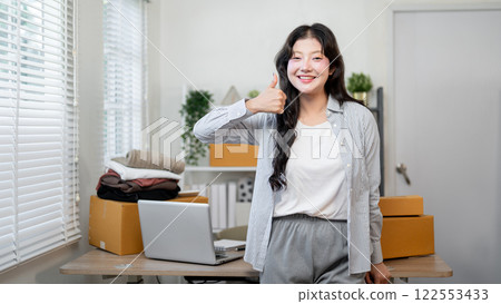 A confident Asian female business entrepreneur stands in office, showing her thumb at the camera. 122553433