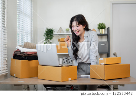 Smiling Asian female business owner is happy with the large number of orders, working in her office. 122553442
