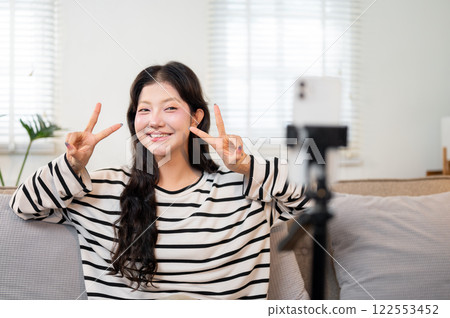 A confident Asian female content creator is recording a video from her living room. A confident Asian female content creator is recording a video from her living room. 122553452