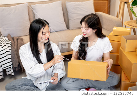 Two Asian women are packing items into cardboard boxes, running a small online business together. 122553743