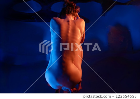 Woman in artistic nude pose in a softly lit studio with blue hues 122554553