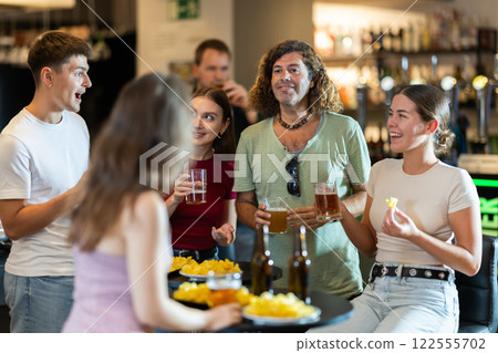 Happy mens and womens drinking beer and eating crisps, laughing and spending time together in bar 122555702