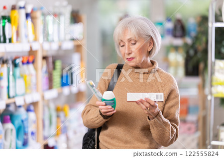 Portrait of an elderly woman choosing mouthwash and toothbrush in supermarket 122555824