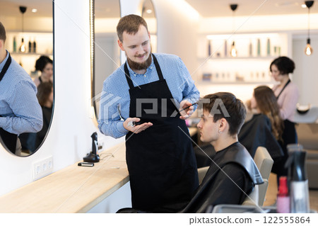 Young male hairdresser giving haircut to young guy 122555864
