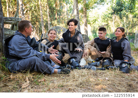 Positive paintball players sitting on battleground and chatting 122555914