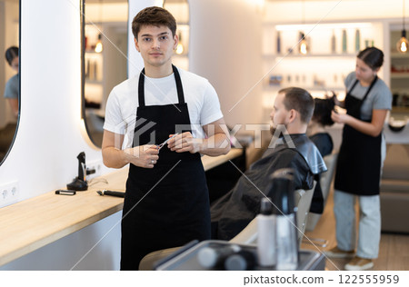 Guy hairdresser stylist stands near workplace with tool in hands. 122555959