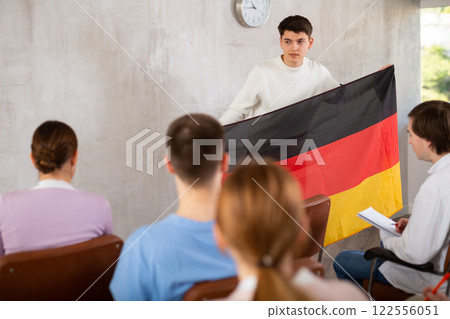 Young male professor showing german flag to group of students Young male professor showing german flag to group of students 122556051