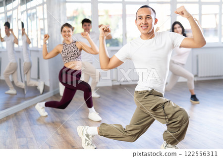 Positive woman and man engaged in dancing in group practices energetic swing in dance studio 122556311