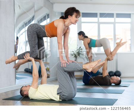 Athletic man balancing woman in his feet during acro yoga practice in fitness center Athletic man balancing woman in his feet during acro yoga practice in fitness center 122556465