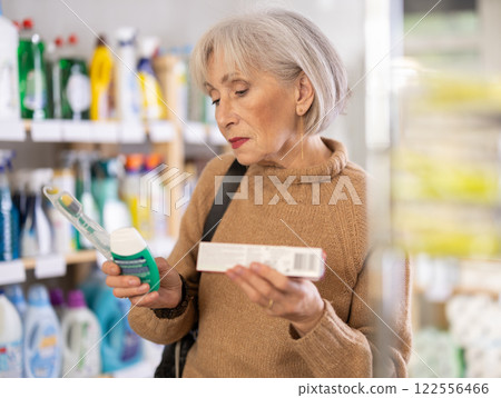 Portrait of an elderly woman choosing mouthwash and toothbrush in supermarket 122556466
