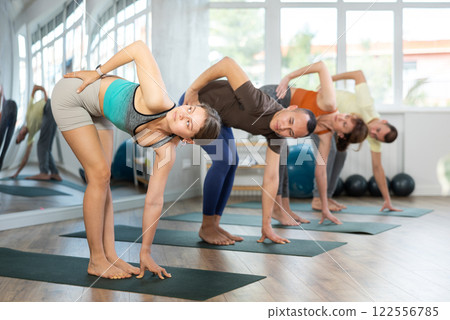 Happy woman standing on yoga mat with group of sporty people practicing yoga lesson at sport studio Happy woman standing on yoga mat with group of sporty people practicing yoga lesson at sport studio 122556785