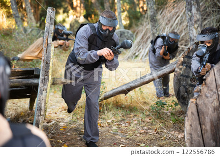 Paintball players aiming and shooting with guns at opposing team Paintball players aiming and shooting with guns at opposing team 122556786