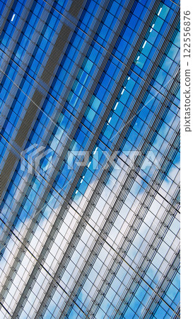 An abstract close-up of a glass skyscraper with diagonal lines, blue tones, and reflections of clouds. Highlights geometric precision and the dynamic interplay between architecture and the sky An abstract close-up of a glass skyscraper with diagonal lines, blue tones, and reflections of clouds. Highlights geometric precision and the dynamic interplay between architecture and the sky 122556876