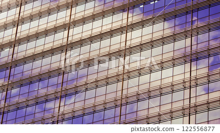 A facade of a modern skyscraper reflecting warm tones of sunset in its windows, interspersed with parallel metallic gridlines. A blend of urban architecture and the natural light soft hues A facade of a modern skyscraper reflecting warm tones of sunset in its windows, interspersed with parallel metallic gridlines. A blend of urban architecture and the natural light soft hues 122556877