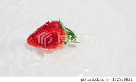 A vibrant red strawberry with a green leafy top is captured mid-splash in liquid, set against a smooth white background for a clean, fresh look. A vibrant red strawberry with a green leafy top is captured mid-splash in liquid, set against a smooth white background for a clean, fresh look. 122556921