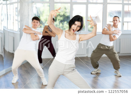 Happy enthusiastic young girl honing hip-hop moves in dance studio setting with group of women and men 122557056