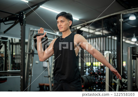 A strong Asian man is performing a clean and press with a kettlebell, exercising in the gym. A strong Asian man is performing a clean and press with a kettlebell, exercising in the gym. 122558103