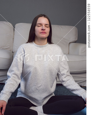 Woman practicing yoga, sitting cross-legged on floor, engaging in mindful breathing and meditation for stress relief and inner calm vertical photo 122558559