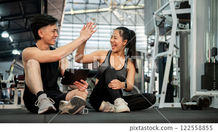 A cheerful male fitness trainer and his female client are in the gym, giving each other a high five A cheerful male fitness trainer and his female client are in the gym, giving each other a high five 122558855