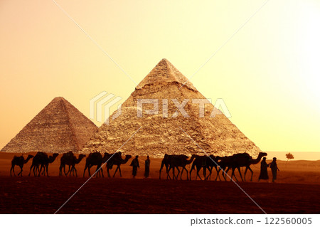 Horizontal banner with caravan of camels and Great Pyramids of Chephren and Cheops, Cairo, Egypt. People with dromedaries and three pyramids, Giza complex (Giza Necropolis). On sunrise sky background 122560005