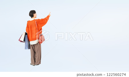 Full-body photo of a stylish middle-aged woman holding a shopping bag and pointing Full-body photo of a stylish middle-aged woman holding a shopping bag and pointing 122560274