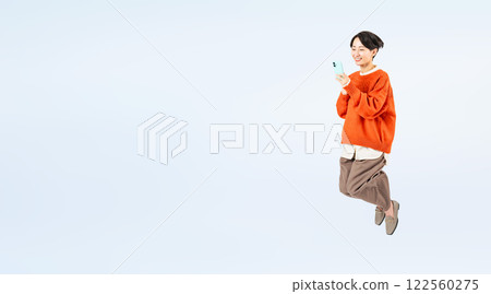 一位時尚中年女性一邊看著智慧型手機一邊跳躍的全身照片 122560275