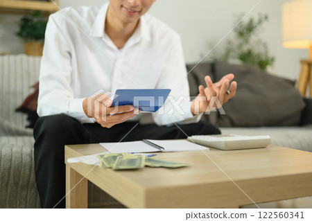Smiling adult man sitting in a cozy living room checking his bankbook and calculating expenses 122560341
