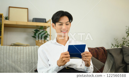 Young man sitting on a couch and reviewing his bankbook. Finance management concept Young man sitting on a couch and reviewing his bankbook. Finance management concept 122560388