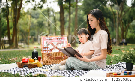 Loving mother and son reading a book during picnic in the park. Outdoor leisure and family bonding concept 122560392