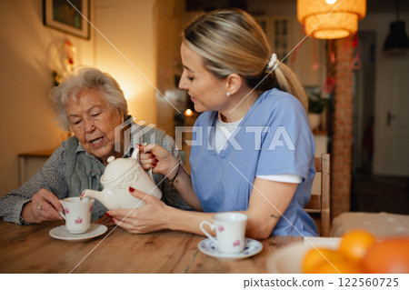 Lovely eldery woman serving tea to friendly caregiver. 122560725